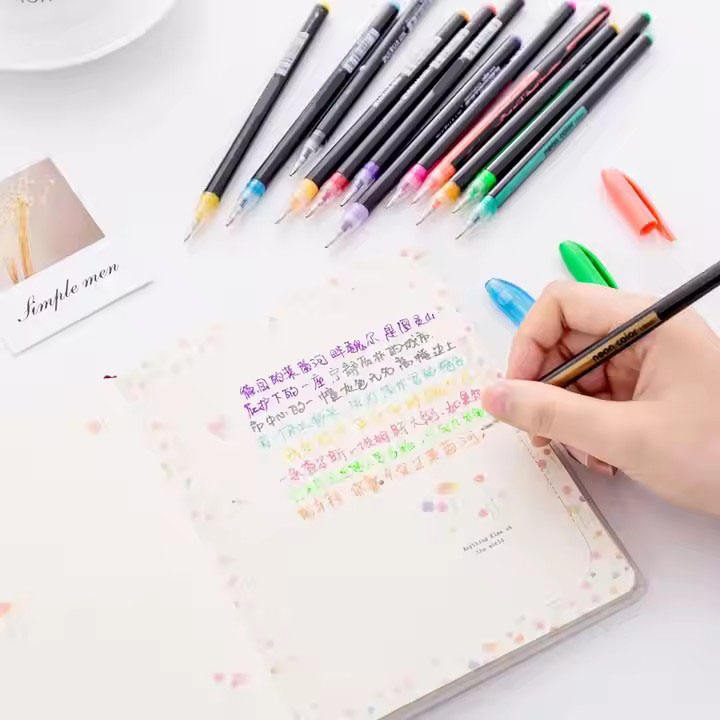 Hand writing in a notebook with colorful markers on a white surface