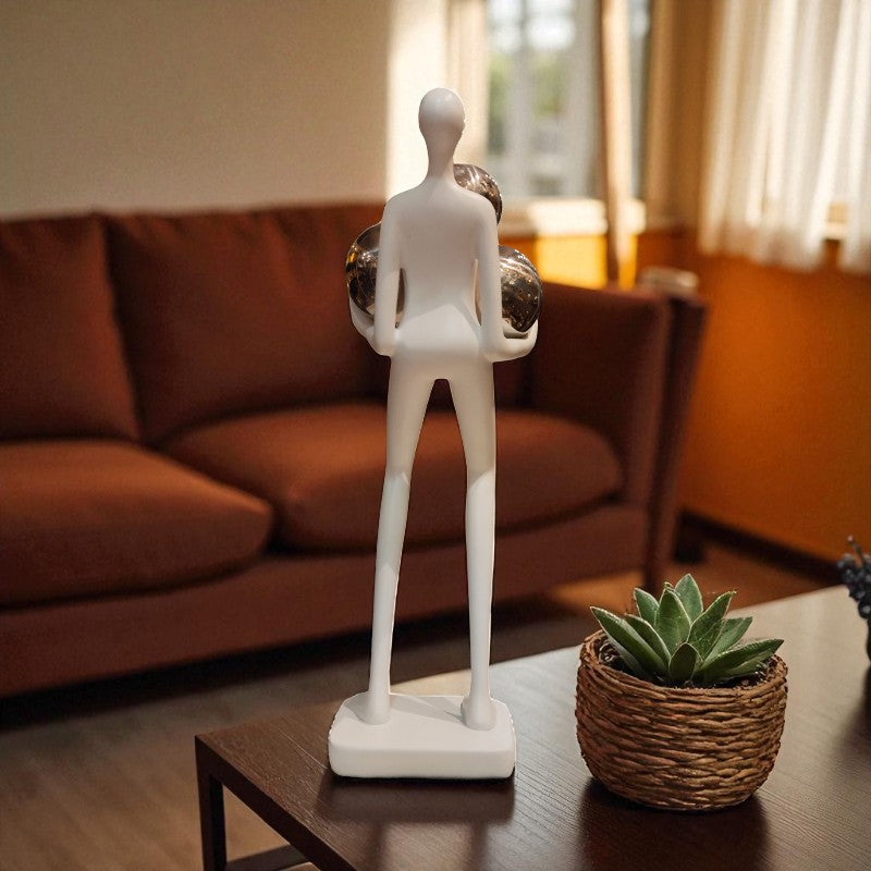 White abstract sculpture on a table with a plant, in a room with a brown sofa and window.