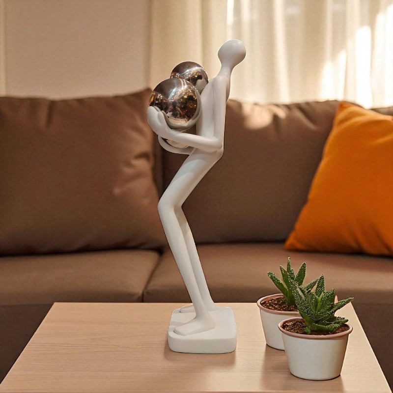 Decorative sculpture of a person holding a globe on a coffee table with potted plants.