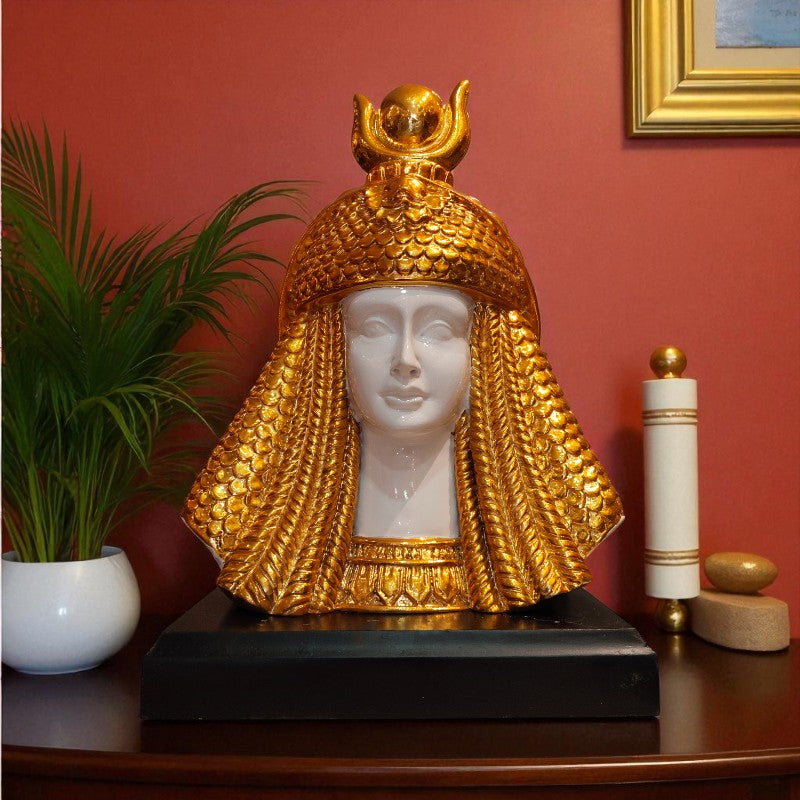 Decorative bust with gold headdress on a wooden surface against a red wall.