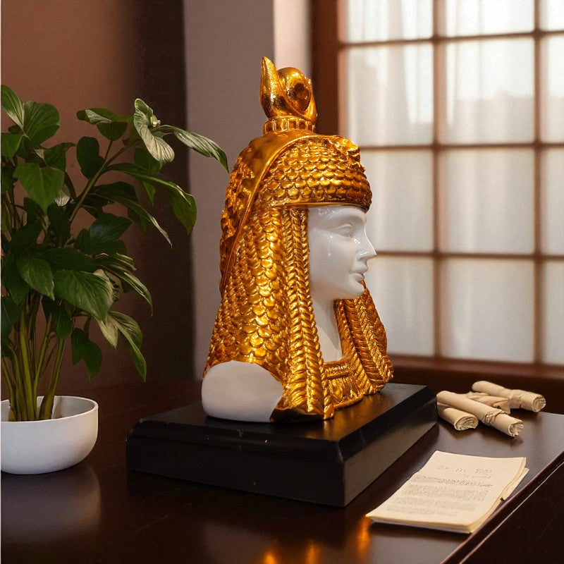 Decorative statue of a figure with gold headgear on a table with a plant and papers.