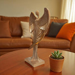 Decorative angel sculpture on a table with a potted plant, in front of a brown sofa.