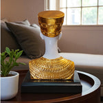 Decorative object with gold and white design on a table with a plant and sofa in the background