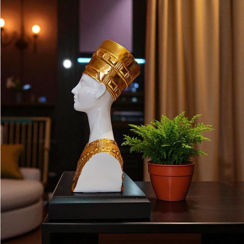Statue of a head with gold headdress on a table with a plant in the background