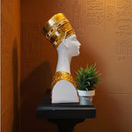 Bust with gold headpiece on a pedestal against an Egyptian hieroglyphs wall.