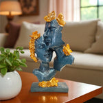 Decorative sculpture of a face with gold accents on a table in a living room setting.