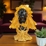 Decorative statue with gold and black finish on a wooden surface with a plant in the background