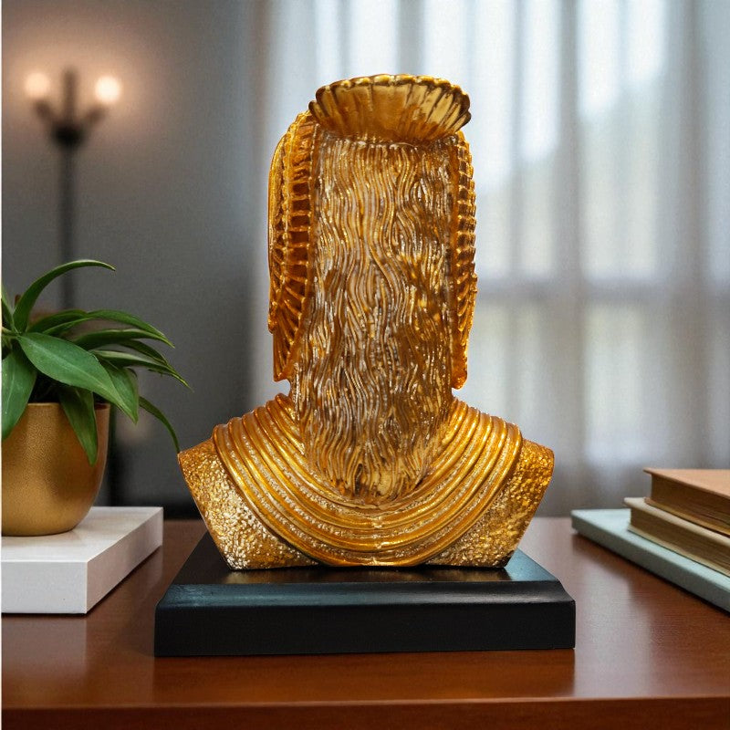 Gold decorative bust on a wooden surface with a plant and books in the background