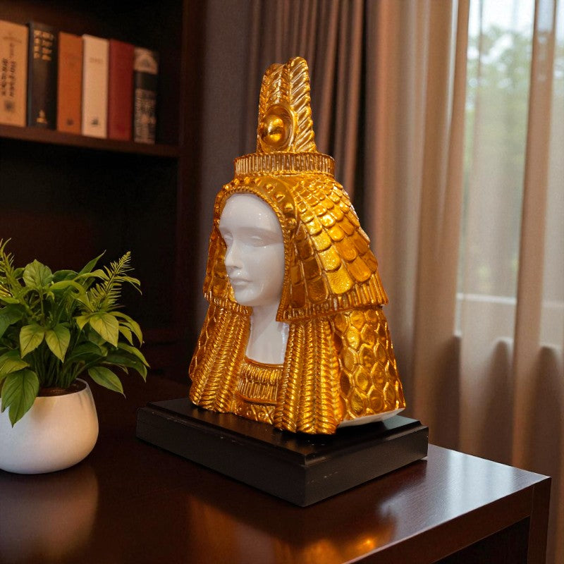 Decorative golden head sculpture on a table with a plant and books in the background