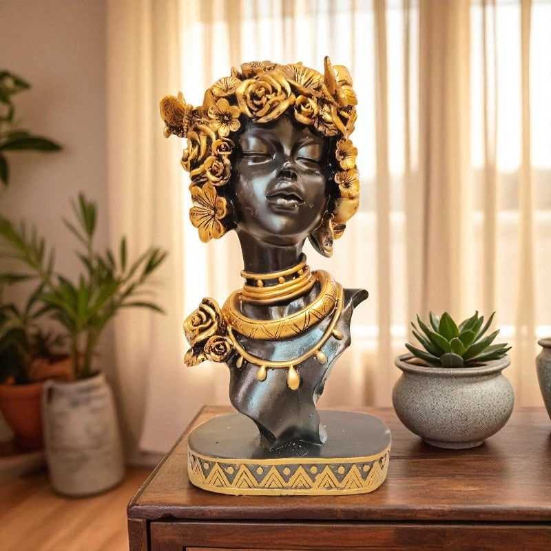 Decorative bust with gold accents on a wooden table with plants in the background