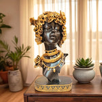 Decorative bust with gold accents on a wooden table with plants in the background