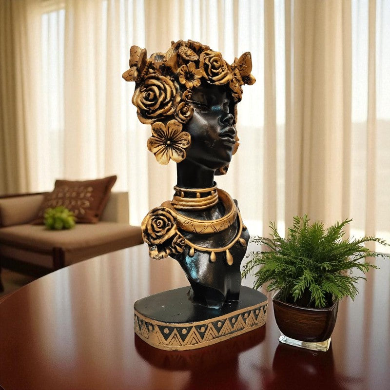 Decorative bust with floral and jewelry details on a table in a room with curtains and plants.