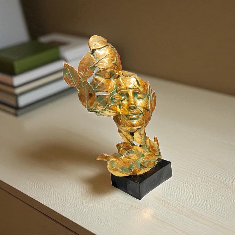 Gold decorative sculpture of a face with leaves on a wooden surface