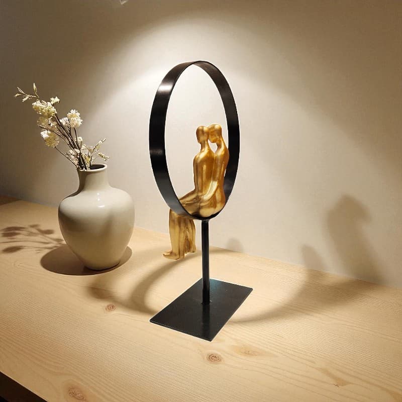 Decorative sculpture of a couple in a circle with a white vase on a wooden surface.