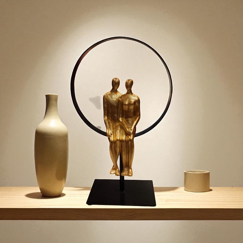 Decorative sculpture of two figures embracing on a stand with a vase and small container on a wooden surface.