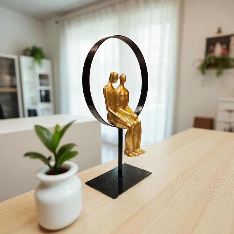 Decorative sculpture of two figures sitting on a black circular stand on a table with a blurred indoor background.