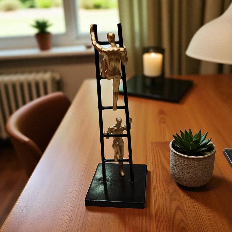 Decorative ladder sculpture with gold figures on a wooden table.