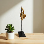 Decorative sculpture on a black stand next to a potted plant on a wooden surface.