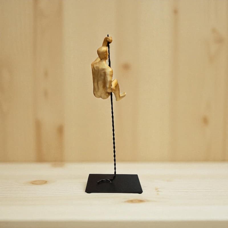 Gold climbing figure on a black stand against a wooden background