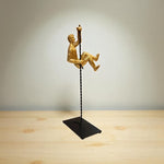 Gold sculpture of a person on a swing against a plain background