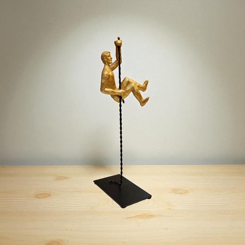 Gold sculpture of a person on a swing against a plain background