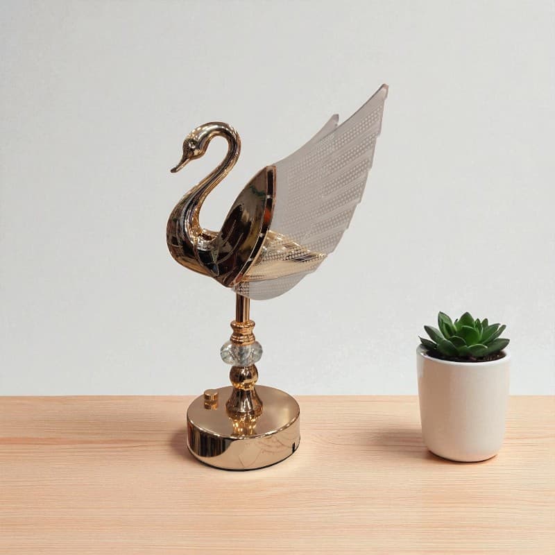 Decorative swan sculpture on a wooden surface with a small potted plant.