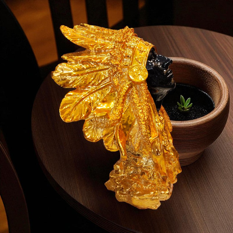 Gold headdress figurine on a wooden surface with a potted plant in the background