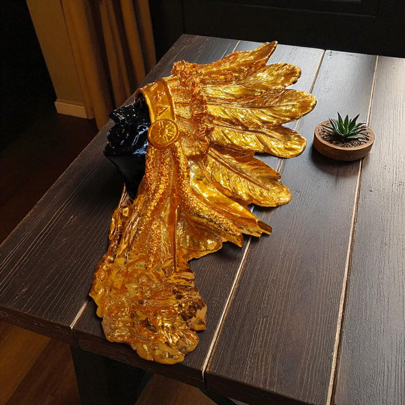 Gold leaf decorative item on a wooden table with a plant in the background