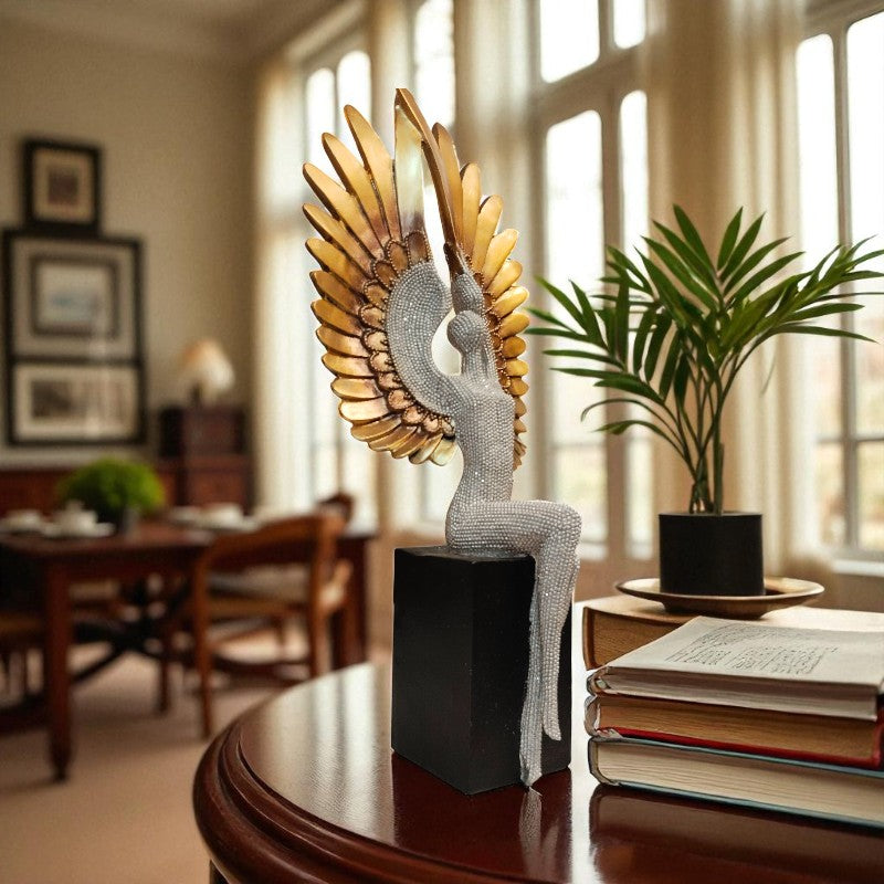 Decorative sculpture of a winged figure on a table with books and a plant in a room.