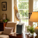 Decorative sculpture on a table with a lamp and chair in a room with large windows.