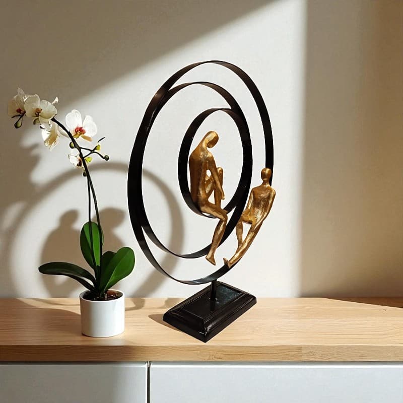 Decorative sculpture of two people on a circular design with a potted orchid on a wooden surface.