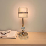 Table lamp with a decorative base on a wooden surface next to an open book and glasses.