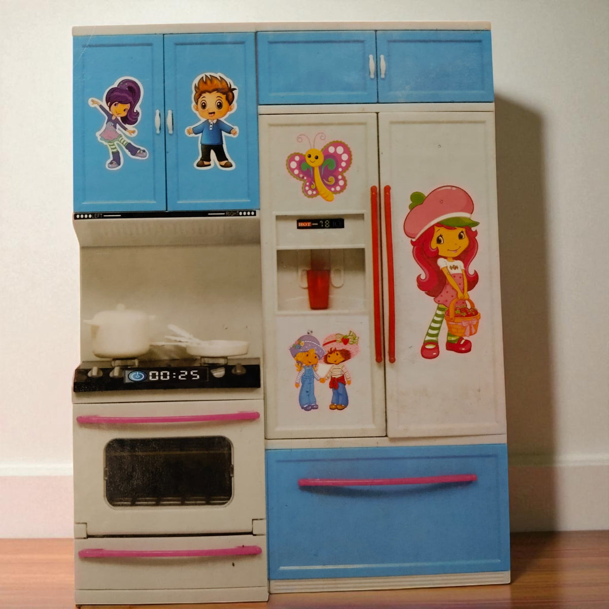 Close up of modern kitchen playset toy with stove, fridge and blue cabinets decorated with cute character stickers.