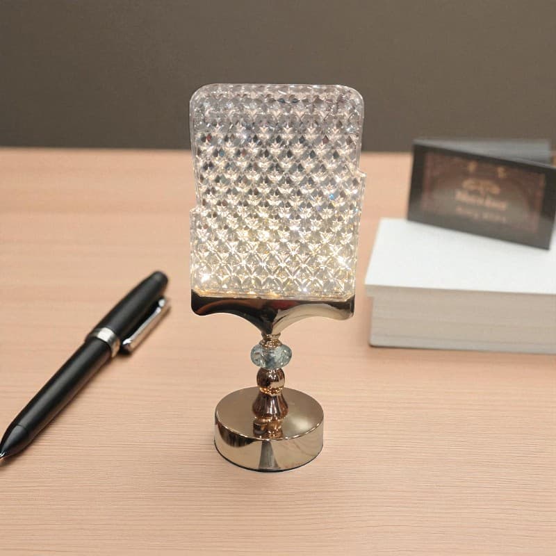 Decorative lamp with crystal design on a wooden surface next to a pen and book.