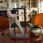 Decorative angel sculpture and potted orchid on a reflective surface with a blurred indoor background.