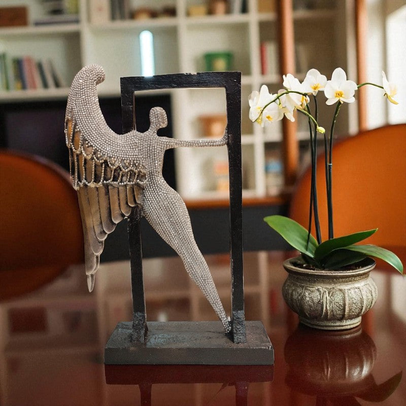 Decorative angel sculpture and potted orchid on a reflective surface with a blurred indoor background.